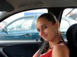 Smiling young woman seated in the driver's side of a car for a driving lesson.